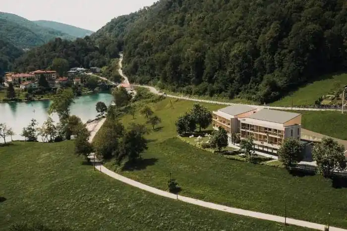 Aerial view of the timber hotel on a meadow above the turquoise Soča, with wooded slopes around it