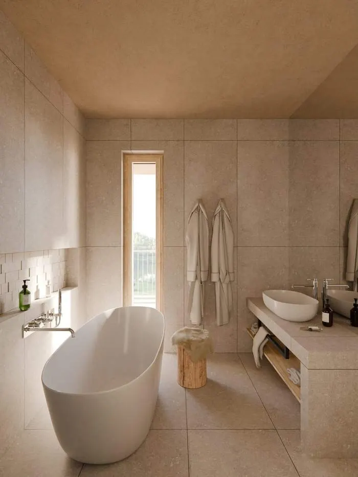 Hotel bathroom in warm stone with a freestanding bath, a tall narrow window and a timber vanity