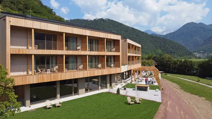 Hotel Tu'lie z leseno fasado in balkoni, v ozadju gore doline Soče